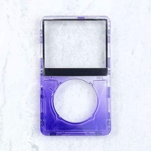 May include: A transparent purple iPod case with a rectangular screen area and a circular button area. The case has a black bar at the top and is made of a clear, durable plastic. The design is simple and functional.
