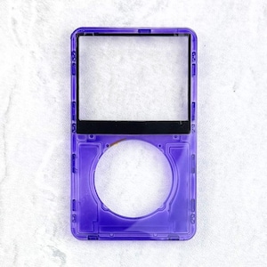May include: A transparent purple electronic device case with a rectangular top section and a circular bottom section. The case has a black bar across the middle and is set against a white background.