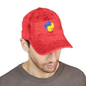 May include: Red baseball cap with a Python logo embroidered on the front. The logo features a blue and yellow snake design on a textured red rectangle. The cap has a curved brim and a distressed, vintage look.