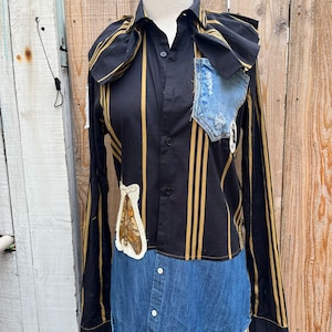 Pode incluir: Uma camisa de manga comprida com listras pretas e douradas e uma parte inferior de ganga. A camisa tem uma grande aplicação de mariposa na frente e um pequeno bolso de ganga no peito.