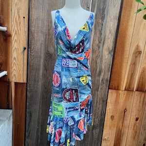 Könnte beinhalten: Ärmelloses Jeanskleid mit Wasserfallausschnitt und Rüschensaum. Das Kleid ist mit Aufnähern mit Text und Grafiken bedeckt. Die Aufnäher enthalten die Wörter "JEANS", "NEW YORK" und "SPECIALTY GOODS".
