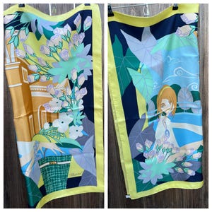 May include: A rectangular silk scarf featuring a yellow border and a multi-colored graphic print. The design includes stylized floral arrangements, a building facade, a green patterned handbag, and a figure with brown hair, with the Chopard logo visible.