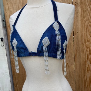 May include: A blue denim halter top with white beaded fringe and silver accents. The top is on a white mannequin.