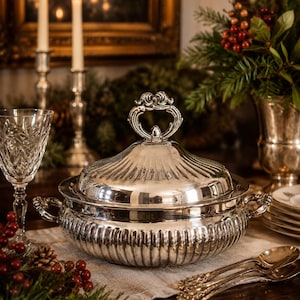 May include: A polished silver serving tureen with a matching lid, featuring vertical fluted detailing along the body and lid. The tureen has two side handles and a decorative ornate finial on top, crafted from a reflective metallic material.