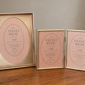 May include: A set of three gold-toned metal picture frames, including one large rectangular frame with an oval mat and a double-hinged frame with two rectangular sections. Each frame contains a pink insert with the text Velvet Relic Studio.
