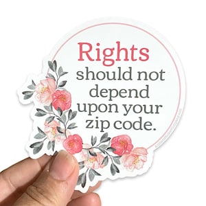 May include: A white circle sticker with a pink floral border. The sticker has the text "Rights should not depend upon your zip code." in black and pink lettering.