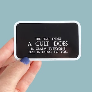 May include: Black and white sticker with the text "THE FIRST THING A CULT DOES IS CLAIM EVERYONE ELSE IS LYING TO YOU."