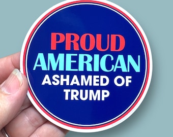 Könnte beinhalten: Ein runder Aufkleber in Blau und Rot mit dem Text "PROUD AMERICAN ASHAMED OF TRUMP" in weißer, roter und blauer Schrift.