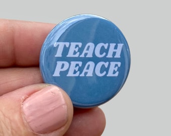 May include: A blue button with white text that reads "TEACH PEACE" in a retro font.
