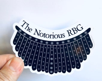 Op de afbeelding: Een witte sticker met een zwarte omtrek van een rechterkraag met de tekst "The Notorious RBG" erop gedrukt.