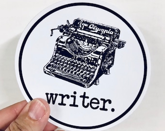 May include: A white round sticker with a black border and a black and white illustration of a vintage typewriter with the text "Olympia" on it. The text "writer." is below the typewriter.