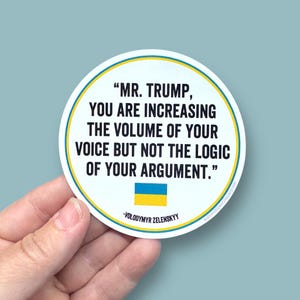 May include: A round sticker with a white background and a blue border. The sticker features a quote in black text: "MR. TRUMP, YOU ARE INCREASING THE VOLUME OF YOUR VOICE BUT NOT THE LOGIC OF YOUR ARGUMENT." The quote is attributed to Volodymyr Zelenskyy. The Ukrainian flag is displayed below the quote.