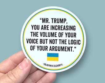 May include: A round sticker with a white background and a blue border. The sticker features a quote in black text: "MR. TRUMP, YOU ARE INCREASING THE VOLUME OF YOUR VOICE BUT NOT THE LOGIC OF YOUR ARGUMENT." The quote is attributed to Volodymyr Zelenskyy. The Ukrainian flag is displayed below the quote.