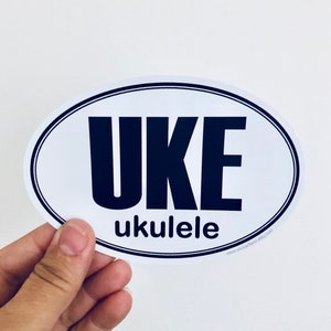 May include: White oval sticker with black text that reads "UKE ukulele" and a website address at the bottom.