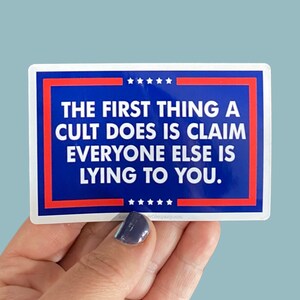 May include: A blue and red sticker with white stars and the text "THE FIRST THING A CULT DOES IS CLAIM EVERYONE ELSE IS LYING TO YOU."