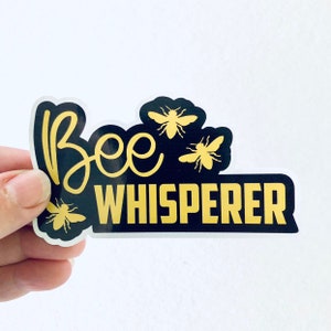 May include: Black and gold sticker with the text "Bee Whisperer" and three stylized bees.