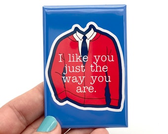 May include: A blue square magnet with a red sweater and white text that reads "I like you just the way you are."