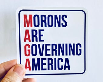 May include: White sticker with blue and red text that reads "MORONS ARE GOVERNING AMERICA".