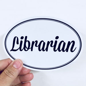 May include: White oval sticker with a black outline and the word "Librarian" written in a black cursive font.