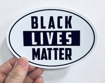 May include: White oval sticker with the text "Black Lives Matter" in black lettering. The word "Lives" is in a black rectangle.