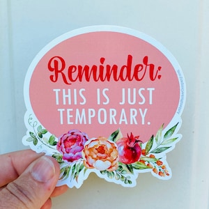 May include: A round sticker with a pink background and the words "Reminder: THIS IS JUST TEMPORARY" in red and white. The sticker is decorated with floral elements in shades of pink, orange, and green.