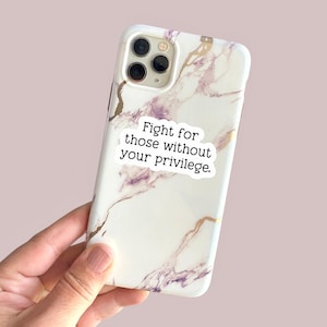 May include: A white phone case with a marble pattern and gold accents. The case has a sticker on it that says "Fight for those without your privilege."