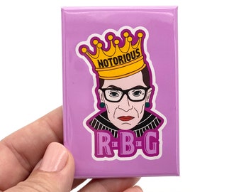 May include: A purple square magnet with a cartoon illustration of Ruth Bader Ginsburg wearing a crown that says "Notorious" and the text "R-B-G".