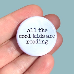 May include: White button with black text that reads "all the cool kids are reading".