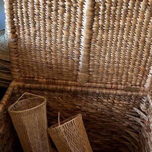 May include: Open wicker trunk with two matching woven baskets inside. The trunk and baskets are made of natural-colored woven material. The trunk has a hinged lid and a metal clasp. The baskets have a flared shape.