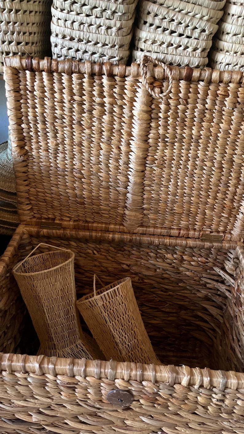 May include: Open wicker trunk with two matching woven baskets inside. The trunk and baskets are made of natural-colored woven material. The trunk has a hinged lid and a metal clasp. The baskets have a flared shape.