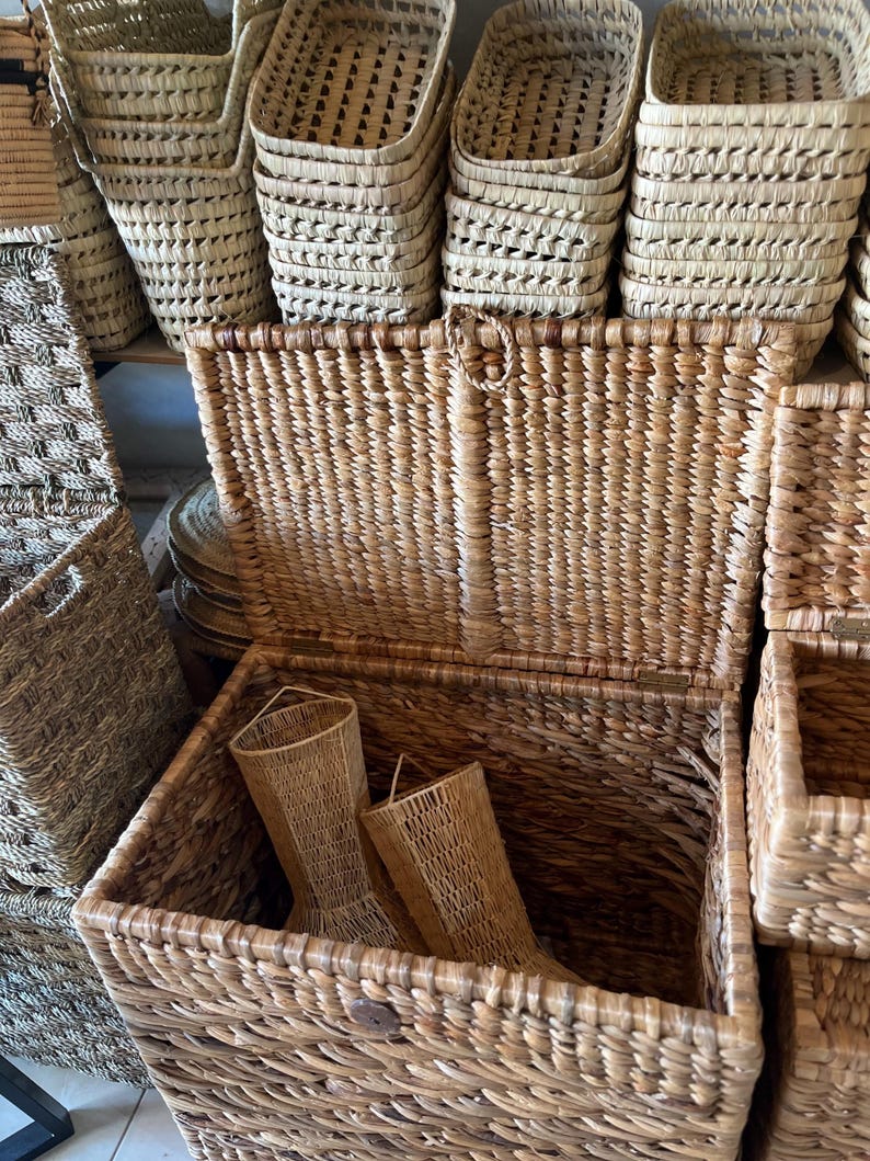 May include: A collection of woven baskets in various sizes and shapes. The baskets are made from natural-colored fibers, with a textured appearance. Some baskets are stacked, while others are open, revealing their interior. The overall aesthetic is rustic and organic.