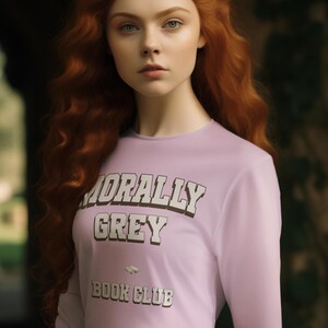 Op de afbeelding: Een vrouw met lang, golvend rood haar en een gouden kroon draagt een lichtpaarse longsleeve met de tekst "MORALLY GREY BOOK CLUB" in het wit. Ze draagt ook een roestkleurige rok.