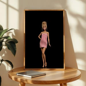 May include: A framed wall art print featuring a blonde doll with an updo hairstyle, wearing a pink strapless towel wrap, standing against a solid black background. The doll has a pink bubblegum bubble in front of its mouth and a hand on its hip.