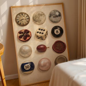 May include: A framed artwork featuring a collection of diverse objects. Includes a clock, moon, disco ball, pomegranate, dice, 8-ball, pearl, grape, wax seal, 10-ball, pink sphere, and bottle cap. The objects are arranged on a beige background.