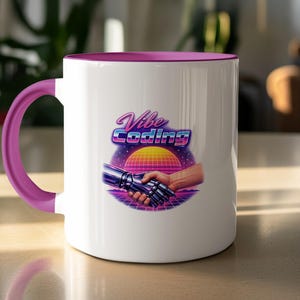 May include: White ceramic mug with a purple handle and rim. The mug features the text "Vibe Coding" in a retro font, along with an illustration of a robotic hand shaking a human hand against a sunset background.