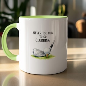 May include: White ceramic mug with a light green handle and interior. The mug features the text "NEVER TOO OLD TO GO CLUBBING" with a golf ball, tee, and club graphic. The mug is designed for golf enthusiasts.