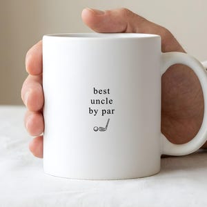 May include: A white ceramic mug featuring the black text "best uncle by par" centered on the front, accompanied by a small black graphic of a golf ball and a golf club positioned directly below the text.