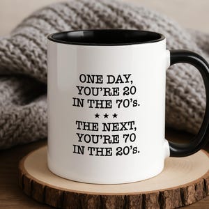 Può includere: Una tazza in ceramica bianca con interno e manico neri. Sulla parte anteriore della tazza è presente un testo nero che recita: ONE DAY, YOU'RE 20 IN THE 70'S. *** THE NEXT, YOU'RE 70 IN THE 20'S. La tazza ha una forma cilindrica e una finitura liscia.