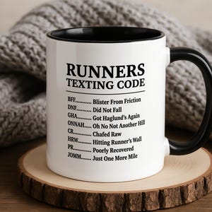 Peut inclure: Un mug en céramique blanche avec un intérieur et une anse noirs, présentant le texte imprimé en noir RUNNERS TEXTING CODE suivi d'une liste d'acronymes liés à la course à pied et leurs définitions, incluant BFF, DNF, GHA, ONNAH, CR, HRW, PR et JOMM.