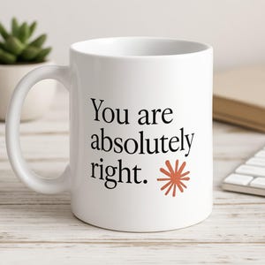 Könnte beinhalten: Ein weißer Keramikbecher mit dem schwarzen Aufdruck "You are absolutely right.", gefolgt von einer kleinen, rostfarbenen, sternförmigen Grafik. Der Becher hat einen glatten, zylindrischen Körper und einen geschwungenen Henkel auf der linken Seite.