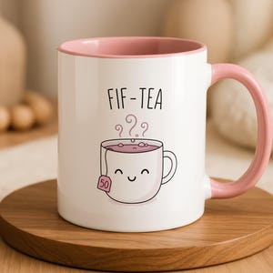 White mug with pink handle and rim, featuring a smiling tea bag illustration.