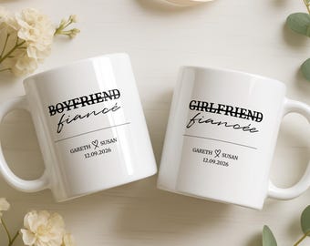 Op de afbeelding: Twee witte keramische mokken met zwarte tekst. Eén mok bevat de tekst BOYFRIEND fiancé met GARETH ♡ SUSAN 12.09.2026. De andere mok bevat de tekst GIRLFRIEND fiancée met GARETH ♡ SUSAN 12.09.2026. Beide mokken zijn voorzien van een handvat.