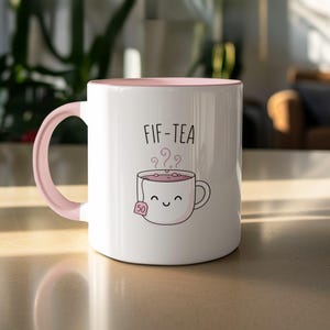 White mug with pink handle, "Fifi-Tea" text and a smiling teabag graphic.