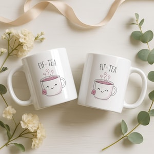 Two white mugs with smiling tea bags saying "FIF-TEA".