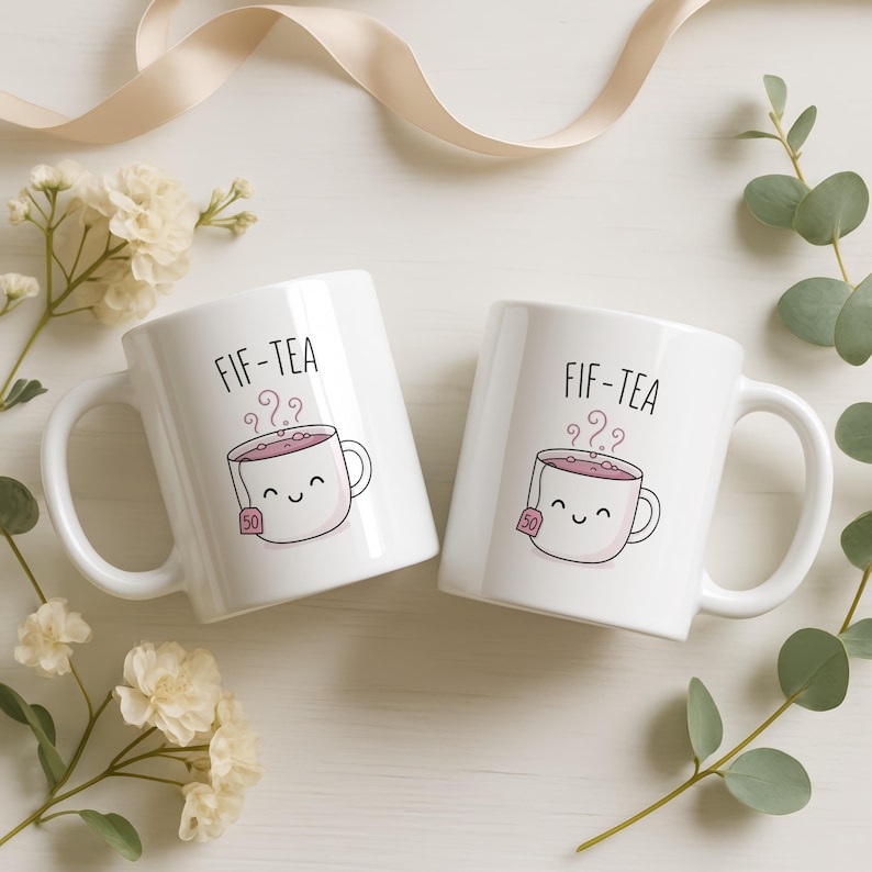 Two white mugs with smiling tea bags saying "FIF-TEA".