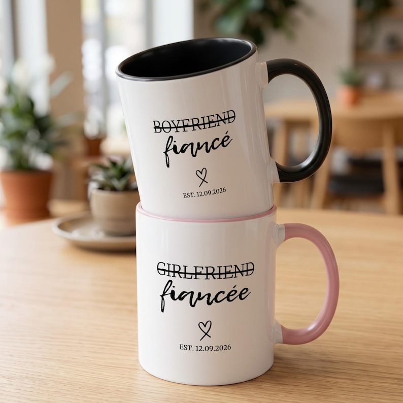 Two white mugs stacked, one says "Boyfriend Fiancé", the other "Girlfriend Fiancée".
