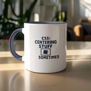 May include: White ceramic mug with a navy blue handle and rim. The mug features the text "CSS: CENTERING STUFF SOMETIMES" in navy blue, along with a graphic of a square. The mug is sitting on a light-coloured surface.
