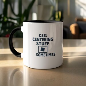Peut inclure: Mug en céramique blanche avec une anse et un intérieur noirs. Le mug affiche le texte "CSS: CENTERING STUFF SOMETIMES" en bleu foncé, ainsi qu'un graphique d'un carré et d'un plus petit carré à l'intérieur.