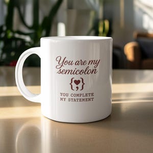 May include: White ceramic coffee mug with a curved handle. The mug features the text "You are my semicolon" in a brown script font, along with a graphic of a semicolon with a heart. Below the graphic, it reads "YOU COMPLETE MY STATEMENT."