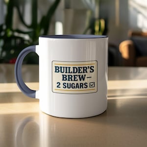 Könnte beinhalten: Weißer Keramikbecher mit marineblauem Innenraum und Henkel. Der Becher zeigt den Text "BUILDER'S BREW - 2 SUGARS" in einem rechteckigen Design. Der Becher steht auf einer hellen Oberfläche.
